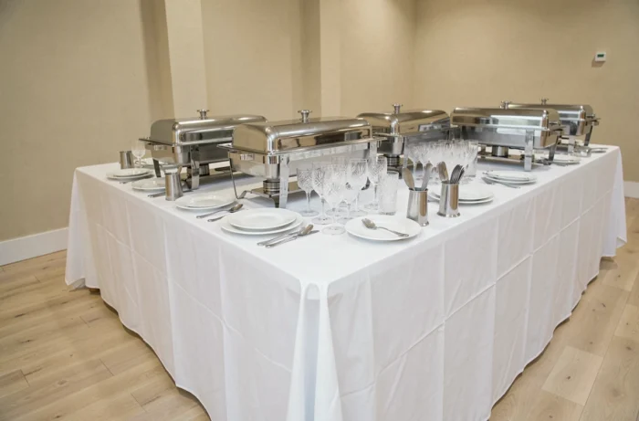 Table de réception professionnelle avec chafing dishes en inox, vaisselle en porcelaine et verrerie cristal pour un événement culinaire élégant